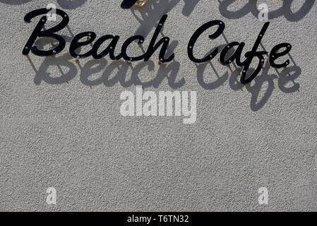 Beach cafe sign casting shadows on grey wall. Stock Photo