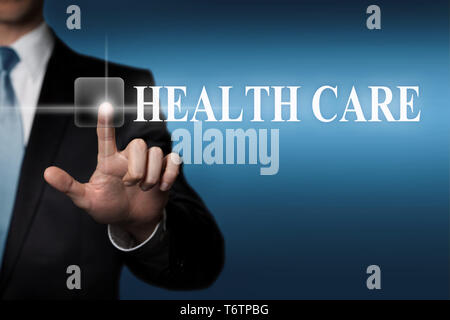 business concept - businessman in suit presses virtual touchscreen button - english word HEALTH CARE Stock Photo