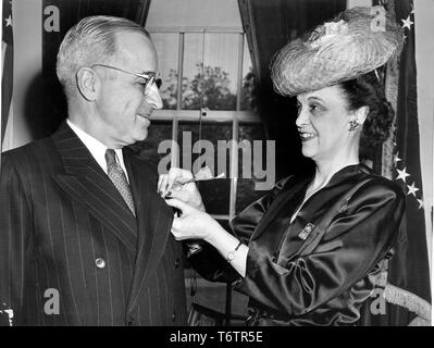Close-up profile view, from the waist up, of Mrs Walter G Craven, National President of the American Legion Auxiliary, pinning a poppy to President Harry Truman's lapel, Washington, DC, April 29, 1946. Image courtesy National Archives. () Stock Photo