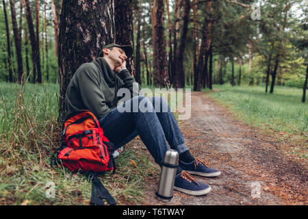 Tired man tourist sleeping in spring forest by tree. Traveler stopped to have rest. Camping, traveling and sport concept Stock Photo