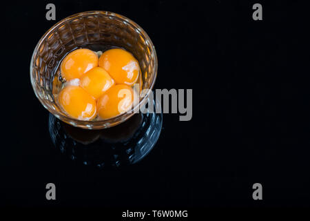 Bright yellow egg yolks in a glass bowl on black background Stock Photo
