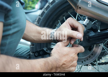 close up technician worker hand, fixed motocycle wheel at the outside of garage. Stock Photo