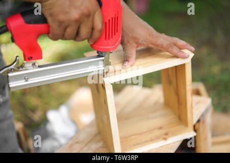 Asian carpenter are shooting the nail by Air Nailer to wooding square box in the backyard garden at home Stock Photo