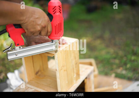 Asian carpenter are shooting the nail by Air Nailer to wooding square box in the backyard garden at home Stock Photo