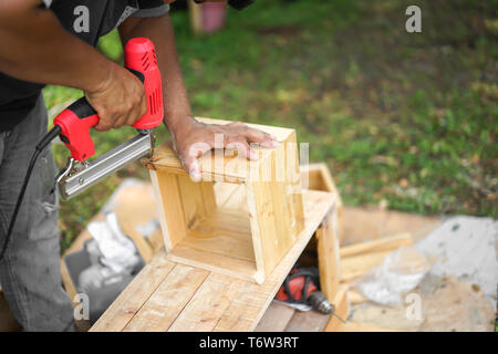 Asian carpenter are shooting the nail by Air Nailer to wooding square box in the backyard garden at home Stock Photo