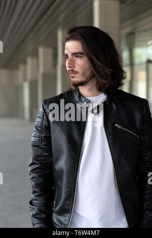 Half length portrait of handsome bearded man dressed in fashionable clothes standing on street against while wall background with area for advertising content. Handsome hipster guy posing on copy space Stock Photo