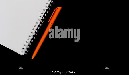 White notebook and orange pen on isolated black background top view Stock Photo