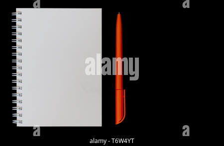White notebook and orange pen on isolated black background top view Stock Photo
