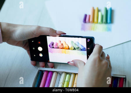 A girl takes on the smartphone multicolored chalks near a picture on a white sheet of paper, background or concept Stock Photo