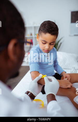 Dark-skinned doctor putting bright plaster on arm for little boy Stock Photo
