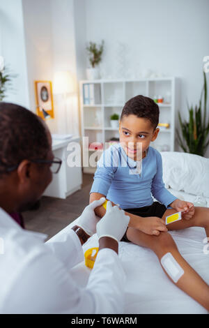 Pleasant boy talking to doctor putting plasters on his body Stock Photo