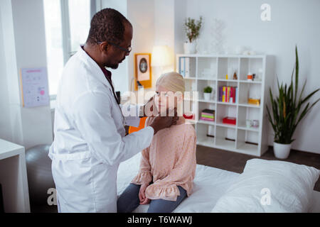 Dark-skinned pediatrician examining throat of little blonde girl Stock Photo
