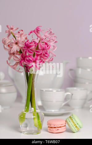 Two macaroons and transparent vase with pink hyacinth flowers on porcelain coffee set background. Selective focus. Tableware concept. Copy space. Vert Stock Photo
