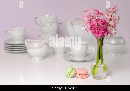Two macaroons and transparent vase with pink hyacinth flowers on porcelain coffee set background. Selective focus. Tableware concept. Copy space. Stock Photo