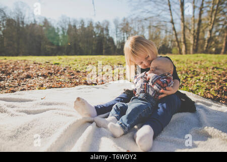 Sister holds her brother while on picnic blanket outside at park