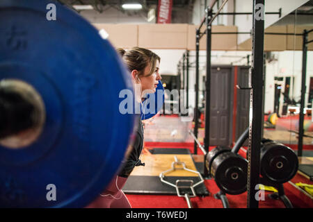 Side view of beautiful woman doing a barbell squat in fitness studio