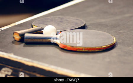 On the grey dusty table are two old battered table tennis rackets and a white plastic ball. Recently, they were used for the game. Stock Photo