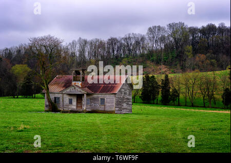 Decaying to the elements, an old school house sits abandoned in a pasture under cloudy skies with misty rain. Stock Photo