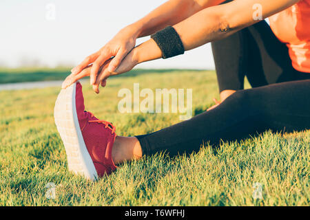 Young runner woman stretching legs before run in a park. Close up athletic and healthy girl wearing white and pink sneakers.