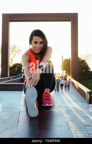 Young runner woman smiling stretching legs before run in a park. Close up athletic and healthy girl wearing white and pink sneakers.
