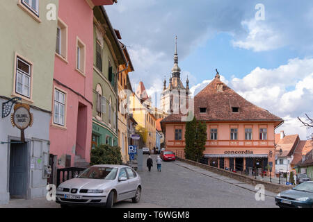 SIGHISOARA, ROMANIA - April 9, 2019: Colorful rooftops and houses in the centre of Sighisoara. Street scene on a sunny day with senior people walking  Stock Photo