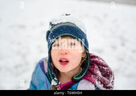 Portrait of a snow-covered little girl standing in the snow with a hat Stock Photo