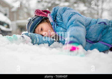 Portrait of a small child laying down on the ground in falling snow Stock Photo