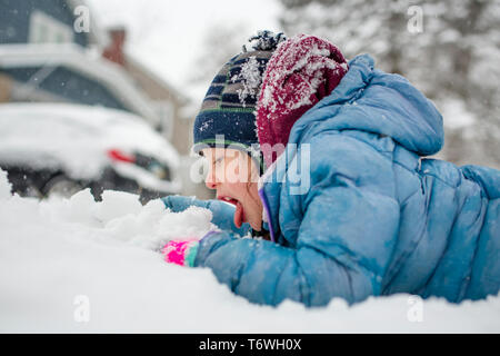 a little girl lays on the ground in falling snow eating snow Stock Photo