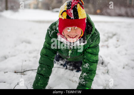 A small snow-covered child in fuzzy hat plays happily in snow