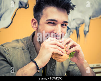 Young man eating a hamburger holding it with his hands Stock Photo