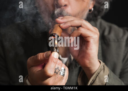 Closeup of hands of a middle aged man lighting up a cigar with a lighter, studio shot Stock Photo