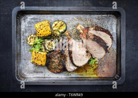 Traditional barbecue veal back racks carree roast with corn and zucchini as top view on an old griddle Stock Photo