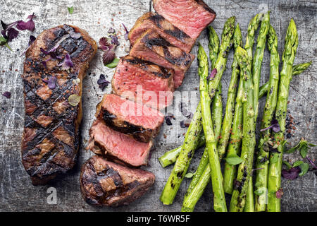 Traditional barbecue dry aged sliced roast beef steak with green asparagus as top view on an old backing form