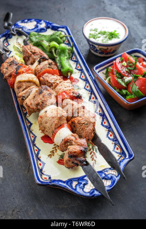 Traditional Greek souvlaki barbecue skewer with tomato onion salad and  tzatziki as closeup on a plate Stock Photo