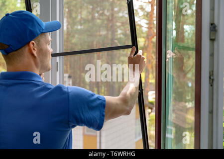 worker installing mosquito net wire mesh in plastic window frame Stock Photo