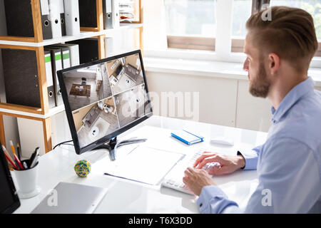 Rear view of security system operator looking at CCTV footage at desk in office Stock Photo