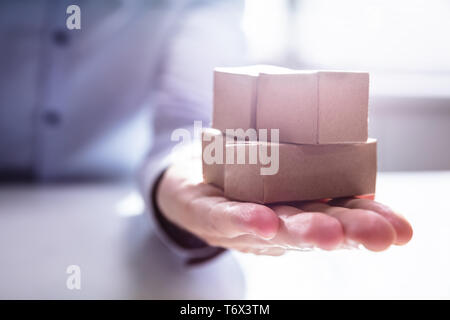Close-up Of Hand Holding Stack Of Miniature Movable Cardboard Boxes On Desk Stock Photo