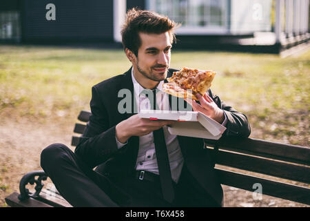 Elegant businessman enjoys eating pizza on his lunch break while sitting outdoor.Toned image. Stock Photo