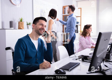 Disabled Man Sitting On Wheelchair Working On Computer In Office Stock Photo