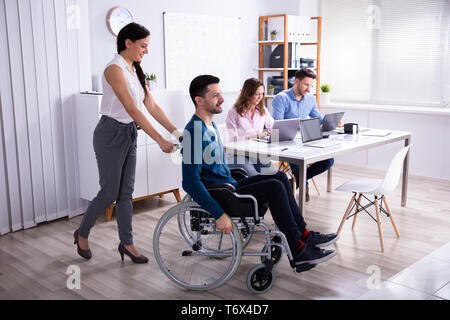 Smiling Young Businesswoman Helping Disabled Colleague In Wheelchair Stock Photo