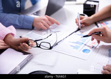 Close-up Of Business Colleagues Working Together With Data Analysis Paper On Desk Stock Photo