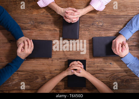 High Angle View Of People's Praying Hands On Holy Bible Stock Photo