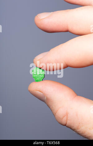 Close-up of caucasian male fingers holding a little green XTC, MDMA, Amphetamine or medication pill on a grey background. Stock Photo
