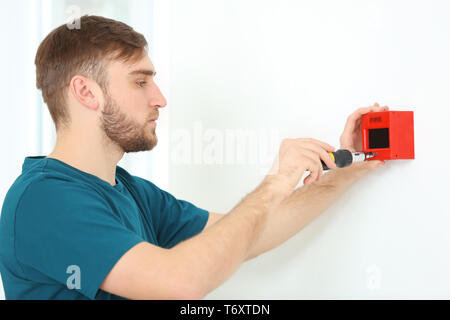 Young electrician installing fire alarm unit on wall Stock Photo