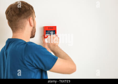 Young electrician installing fire alarm unit on wall Stock Photo