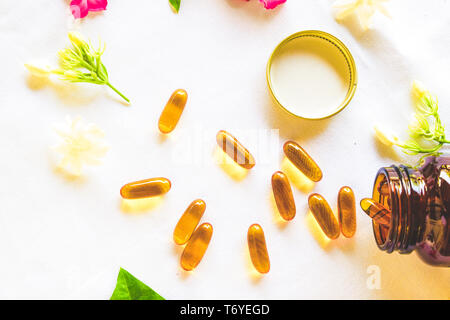 Omega 3 soft gel capsules are decorated with colored flowers over the white fabric background Stock Photo