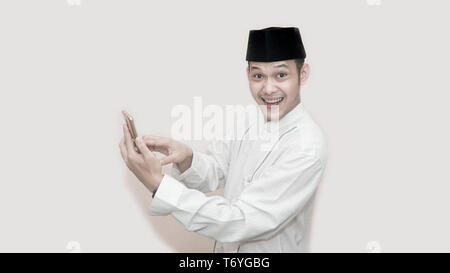 portrait of Funny an asian muslim man with head cap and baju koko taking a call for two way communication -image Stock Photo