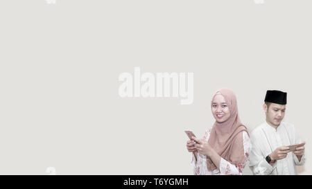 portrait of handsome asian muslim man and women with head cap and scarf using smartphone with copy space ready for your text Stock Photo