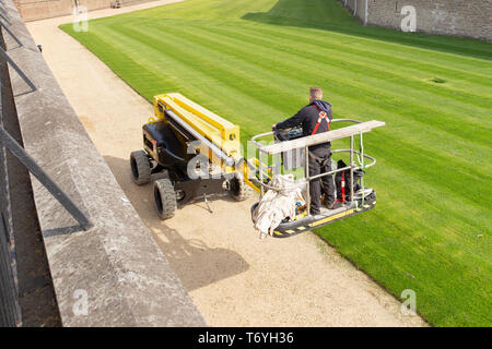 Unidentified gardener cutting the grass of a garden standing on a lawn mower. Stock Photo