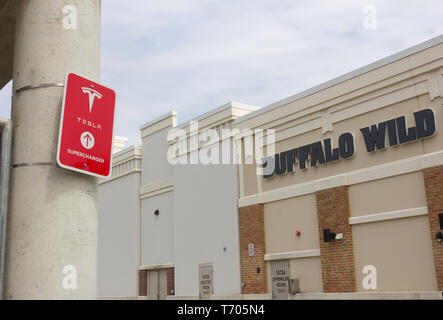 Pictured in April 2019 with a lopped Buffalo Wild Wings restaurant and the backs of stores in the background at the Towne Centre at Laurel shopping center/centre in Laurel, Maryland, USA, is a red 'Tesla Supercharger' sign with logo on a pillar of the parking garage/multi-storey car park where charging stations are located for the California-based automotive company's electric vehicles. The same month, a Tesla Model S caught fire at a Shanghai, China car park due to a faulty battery module in the car. As of June 2019, Tesla had more than 1,500 Supercharger stations worldwide. Kay Howell/Alamy Stock Photo